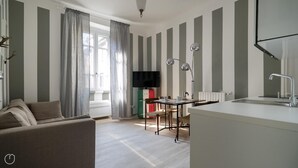 A modern living room with a sofa, a dining table with chairs, a TV, and a kitchen area with a sink and a lamp. - Italianway Easy - Melzo 12 - Righe (Milan)