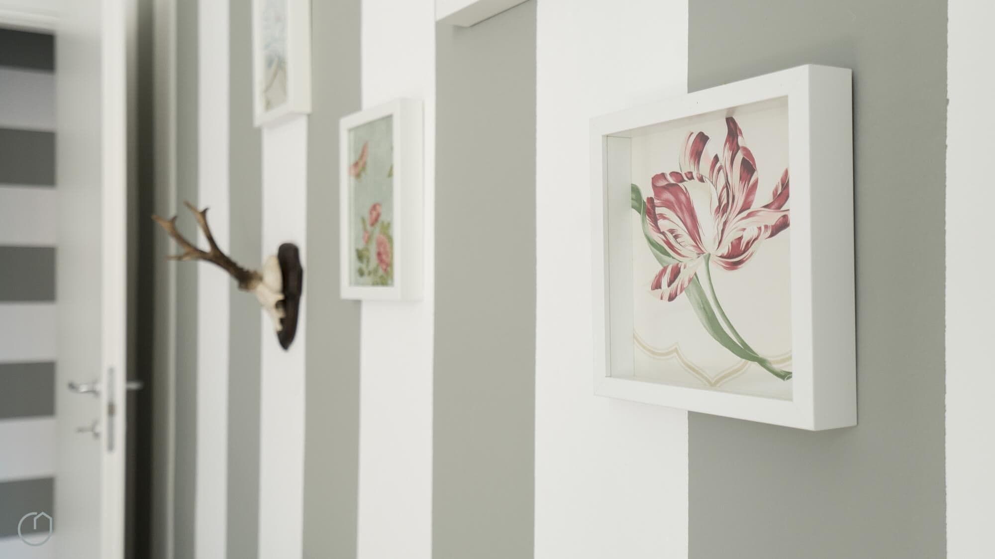 A hallway with framed floral artwork on the wall and a mounted animal head on the left.