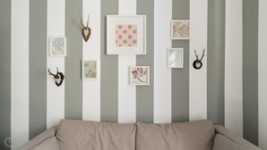 A room with a striped wall, a sofa, and various framed artworks including floral and abstract designs. - Italianway Easy - Melzo 12 - Righe (Milan)