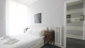 Een hotelkamer met een bed, nachtkastje, radiator en een muur met een ingelijst kunstwerk.