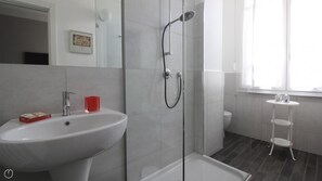 Een moderne badkamer met een douchecabine van glas, een wit wastafel en een klein wit wastafelmeubel.