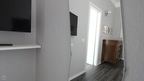 Un couloir avec un téléviseur fixé au mur, une porte donnant sur une autre pièce et un meuble en bois.