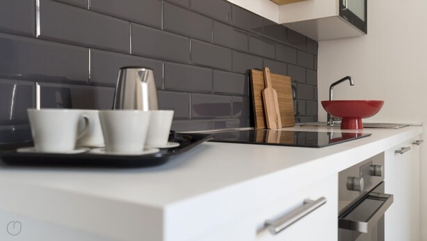 A modern kitchen with a black tiled backsplash, a white countertop, a coffee maker, two white cups, a red bowl, and wooden cutting boards. - Italianway Easy - Melzo 12 - Topolino (Milan)