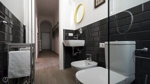 A modern bathroom with a white toilet, a white sink, and a bidet. There is a mirror with a gold frame on the wall, and the floor is tiled. - Italianway Easy - Melzo 12 - Topolino (Milan)