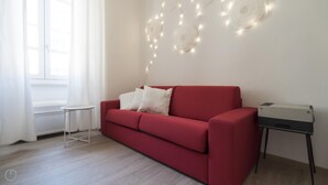 A red sofa with white cushions, a small white side table, and a printer on a black stand. - Italianway Easy - Melzo 12 - Topolino (Milan)