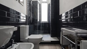 A modern bathroom with black tiled walls, a white toilet, a bidet, and a shower area. - Italianway Easy - Melzo 12 - Topolino (Milan)