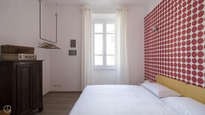 A bedroom with a bed, a dresser, a window with curtains, and a wall with a red and white polka dot pattern. - Italianway Easy - Melzo 12 - Topolino (Milan)