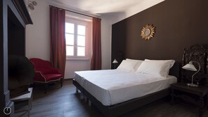 Ett hotellrum med en stor säng, en röd fåtölj, ett skrivbord och ett fönster med gardiner.