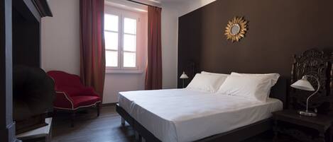 Ein Hotelzimmer mit einem großen Bett, einem roten Sessel, einem Schreibtisch und einem Fenster mit Vorhängen.