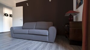 Ett modernt vardagsrum med en grå soffa, ett trägolv, en röd lampa och en dörr med ett handtag.