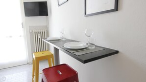 A dining area with a black table, white plates, and clear glasses. There is a yellow stool and a red stool. A white radiator is visible in the background. - Mi-navp112a6 - Naviglio Pavese 112 (Milan)