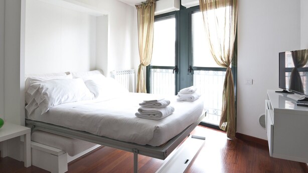 A hotel room with a bed, a desk, a TV, and a window with curtains. - Mi-navp20b1 - Naviglio Pavese 20 II (Milan)