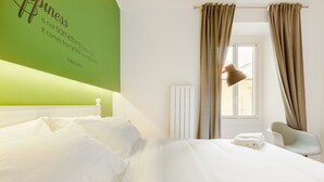A hotel room with a green accent wall, a white bed, a chair, and a window with curtains. - Italianway Easy - Passeroni 2 (Milan)