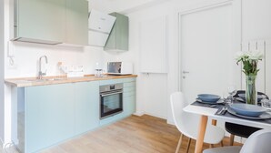 A modern kitchen with light blue cabinets, a built-in oven, and a dining area with white chairs and a table set for two. - Italianway Easy - Passeroni 2 (Milan)