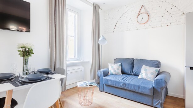 A modern living room with a blue sofa, a dining table set with plates and glasses, a white TV mounted on the wall, and a window with curtains. - Italianway Easy - Passeroni 2 (Milan)