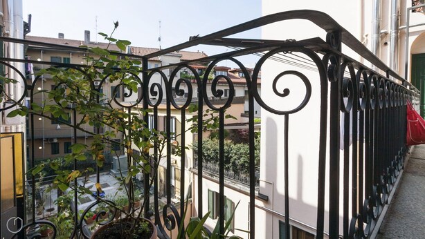 A balcony with a wrought iron railing, potted plants, and a view of neighboring buildings. - Italianway Easy - Pastrengo 11 A (Milan)