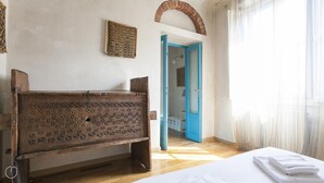 A room with a wooden bench, a bed with white linens, a blue door, and a patterned wall hanging. - Italianway Easy - Pastrengo 11 A (Milan)