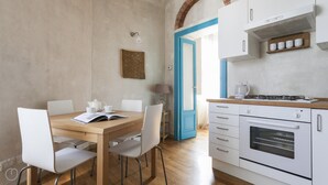 A modern kitchen with white cabinets, a stove, and a coffee maker. There is a dining table with chairs and a book. - Italianway Easy - Pastrengo 11 A (Milan)