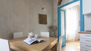 A dining area with a wooden table, white chairs, a white teapot, and a cup. There is a book on the table, and a lamp is on a side table. - Italianway Easy - Pastrengo 11 A (Milan)