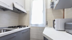 A kitchen with a gas stove, a toaster, and a window with curtains. - Italianway Easy - Petrocchi 48 (Milan)