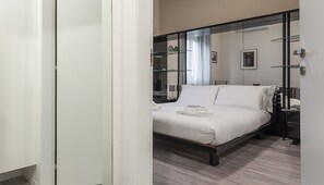 A modern hotel room with a bed, a glass partition, and a nightstand. - Italianway Easy - Petrocchi 48 (Milan)