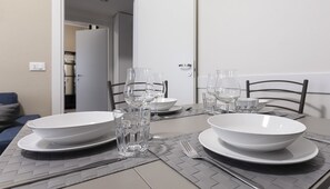 A dining table set with white plates, bowls, and clear glasses, with a woven placemat and metal cutlery. - Italianway Easy - Petrocchi 48 (Milan)