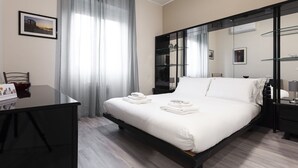 A hotel room with a bed, a desk, a chair, a glass cabinet, and a window with sheer curtains. - Italianway Easy - Petrocchi 48 (Milan)
