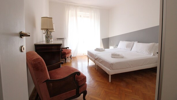 Habitació d'hotel amb un llit, una cadira, una tauleta de nit i una làmpada.