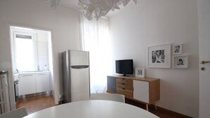 Una cuina moderna amb frigorífic, taula de dinar amb caires i televisor sobre un moble de fusta.