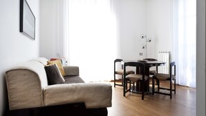 A modern living room with a sofa, a dining table with chairs, and a floor lamp. - Italianway Easy - Piazza Firenze 4 (Milan)