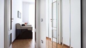 A narrow hallway with a wooden floor, a sofa, and a television in the background. - Italianway Easy - Piazza Firenze 4 (Milan)