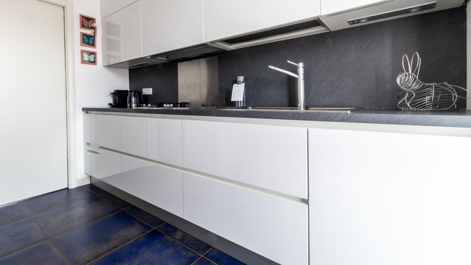 A modern kitchen with white cabinetry, a black countertop, and a decorative wire rabbit sculpture.