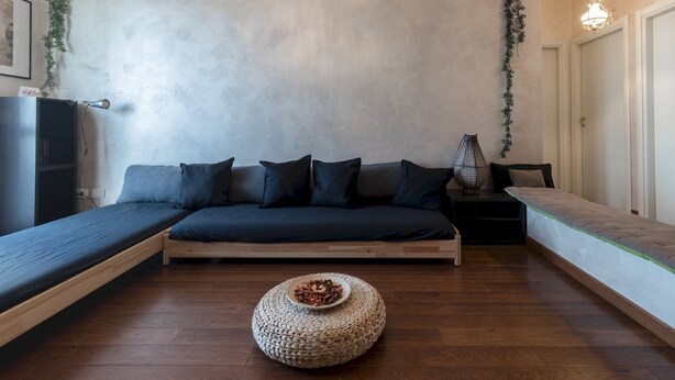 A modern, minimalist room with a built-in sofa, a small round ottoman, and a side table with a lamp. - Mi-pich19a5 - Pichi 19 (Milan)