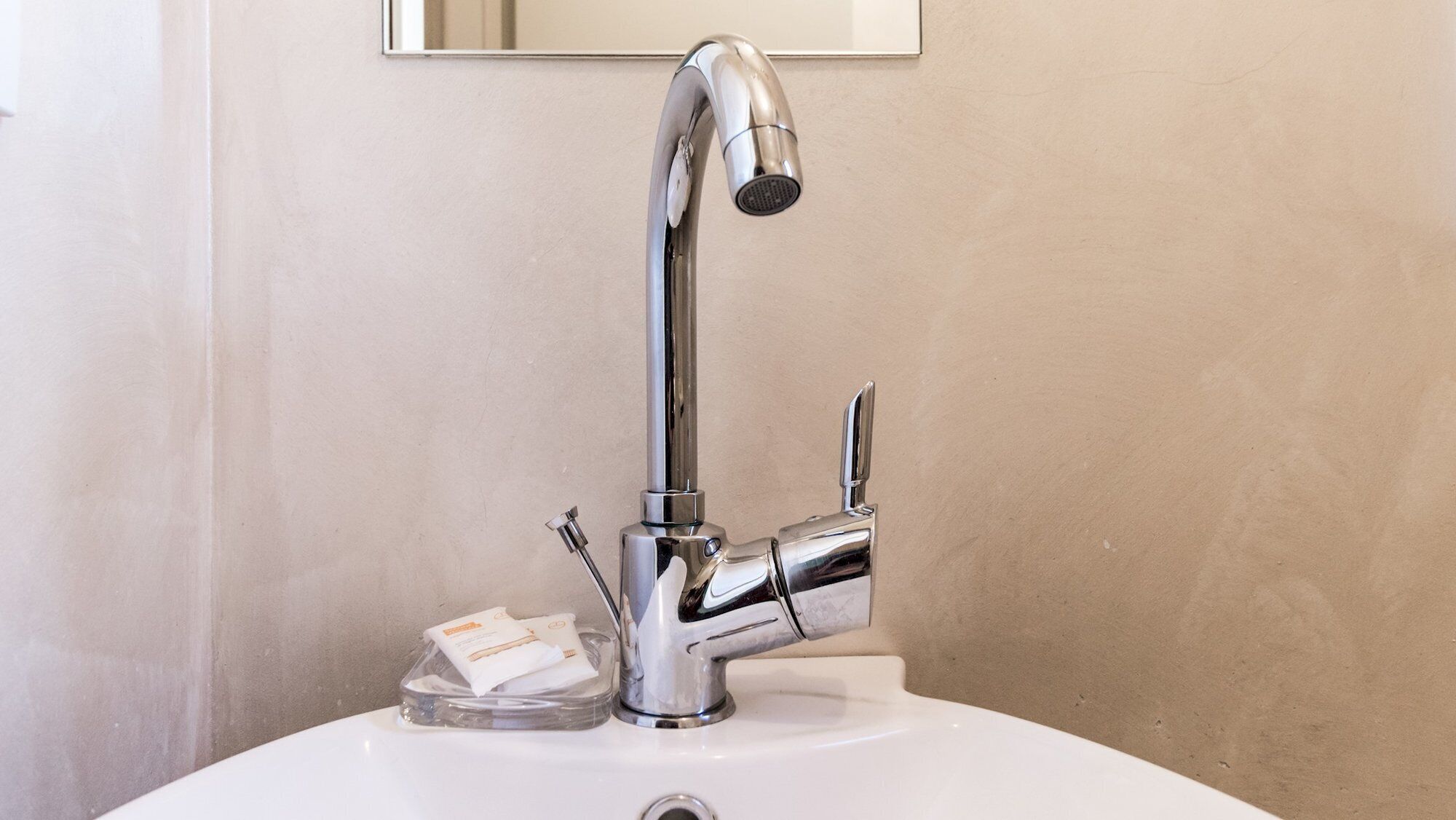 Een wastafel met een chromen kraan en een zeepdispenser.