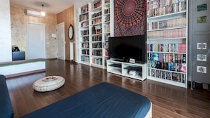 A modern living room with a flat-screen TV, a bookshelf filled with books, a decorative tapestry, and a grey metal cabinet with stickers. - Mi-pich19a5 - Pichi 19 (Milan)