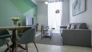 En moderne stue med en grå sofa, et spisebord med stole, et fjernsyn og en vase med blomster.