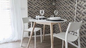 A dining area with a round table, two white chairs, and a patterned wallpaper.