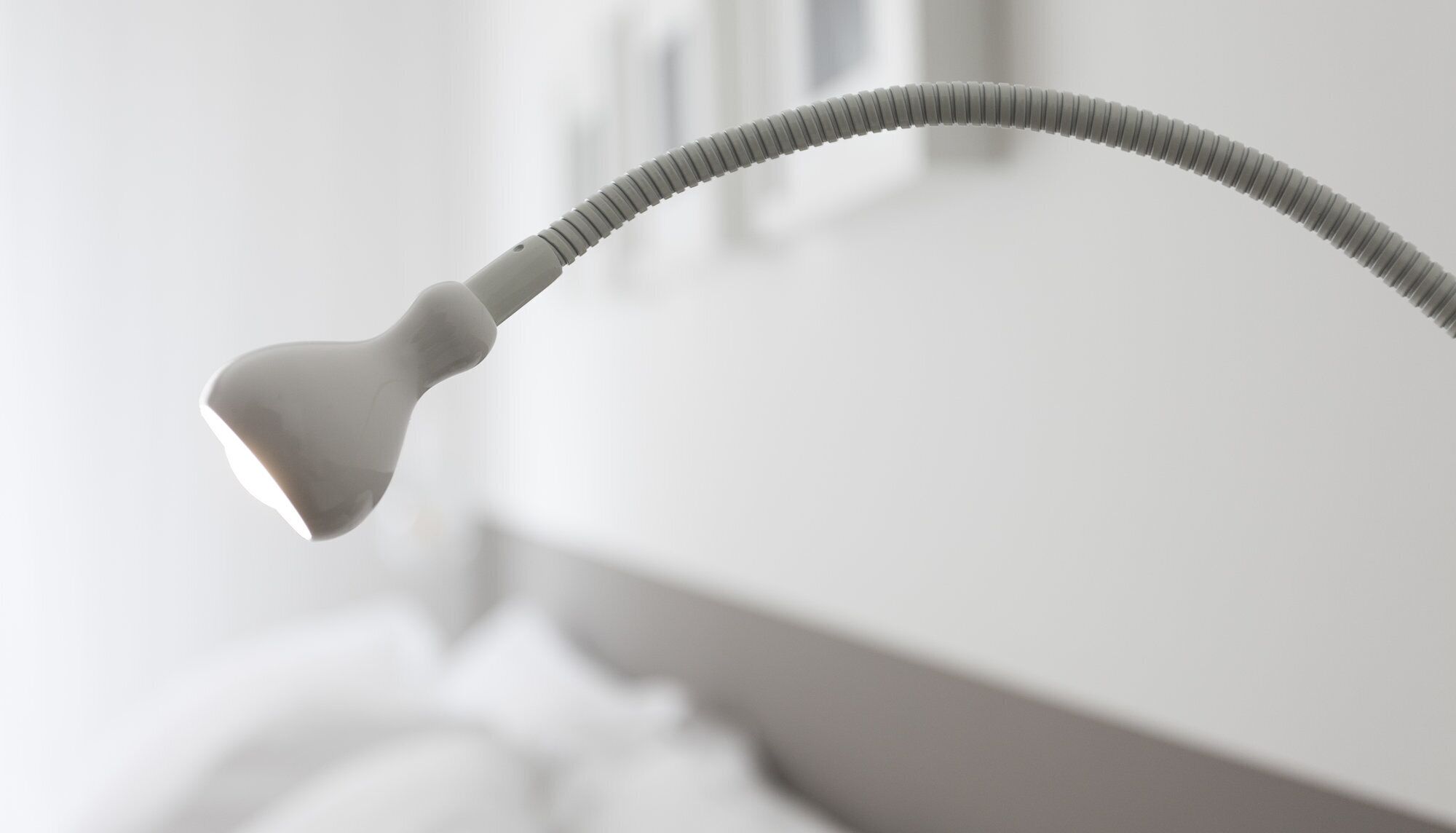 A modern, minimalist lamp with a curved neck and a white shade, positioned on a white surface.