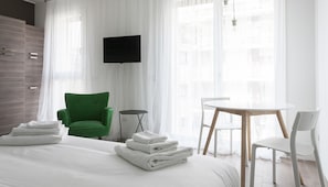 A hotel room with a bed, a green armchair, a small table, and a TV mounted on the wall. - Italianway Easy - Poma 61 S3 (Milan)