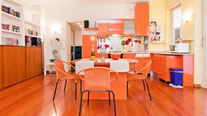 Uma cozinha moderna com armários laranja, uma área de refeições com cadeiras de vime e piso de madeira.