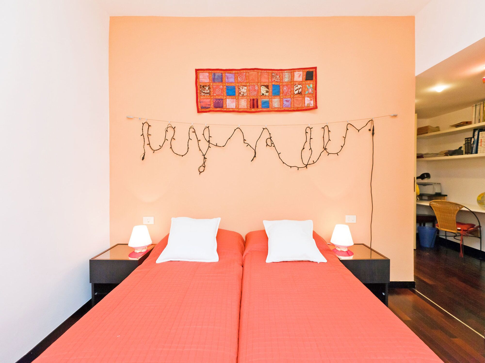 Un letto matrimoniale con una coperta rossa, due cuscini bianchi e un arazzo appeso al muro.
