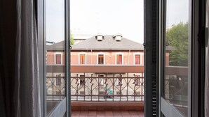 Une vue depuis un balcon doté d’une rambarde en métal, donnant sur un immeuble avec un toit recouvert de tuiles et de nombreuses fenêtres.