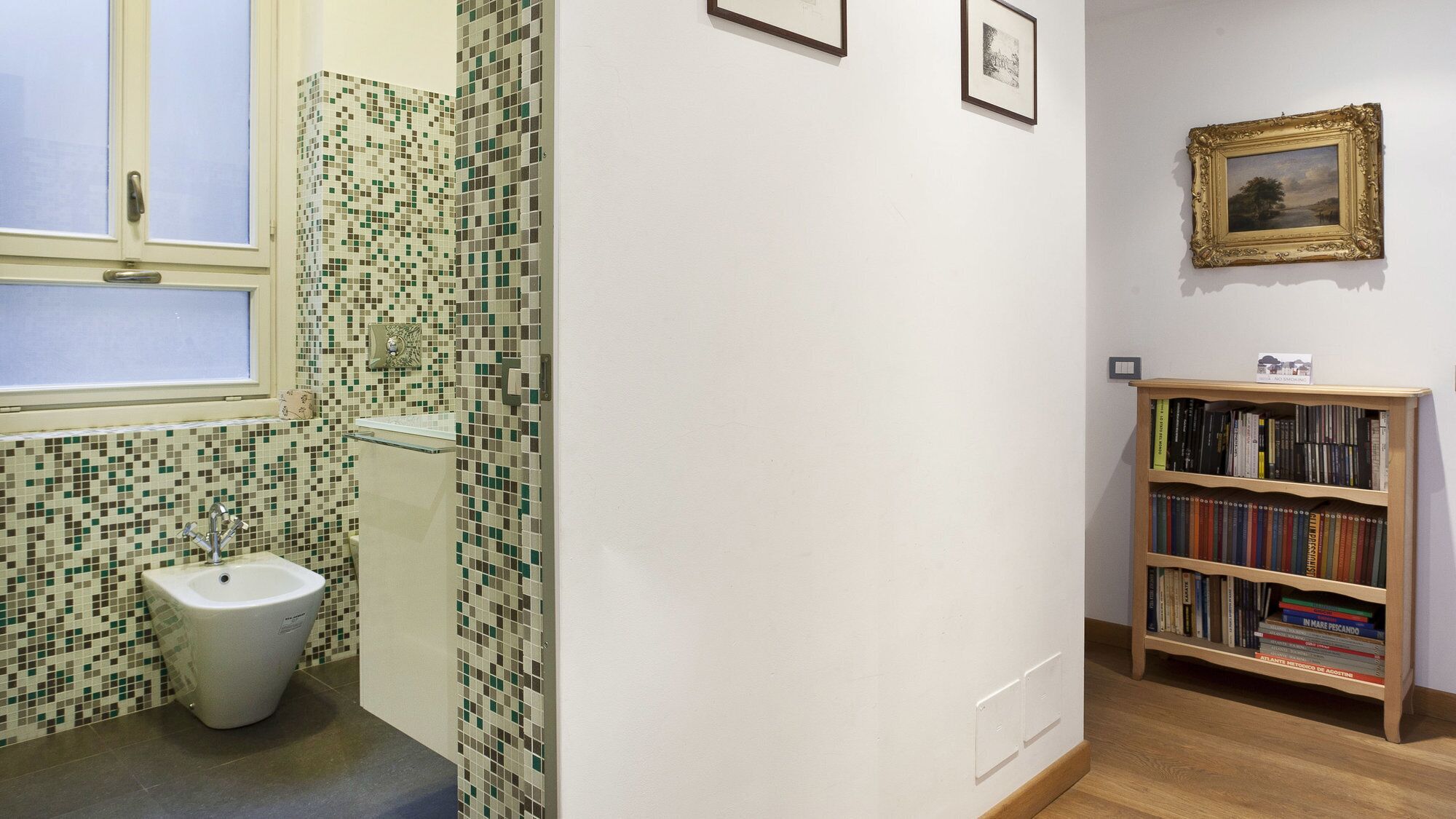 Ein Badezimmer mit Toilette, einem Fenster und einem Bücherregal mit Büchern.