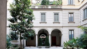 A building with a central entrance flanked by three arches, a balcony with plants, and a door with a red frame. - Italianway Easy - Vincenzo Monti 32 (Milan)