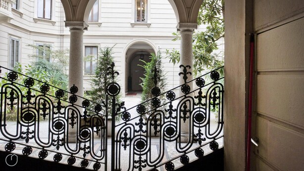 A staircase with ornate black metal railings leading to a courtyard with a building in the background. - Italianway Easy - Vincenzo Monti 32 (Milan)