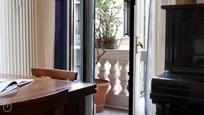 A room with a wooden table, a piano, and a view of a balcony with a potted plant. - Italianway Easy - Vincenzo Monti 32 (Milan)