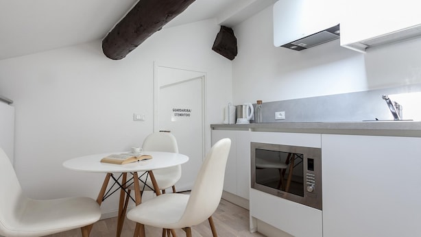 A modern kitchen with white cabinetry, a built-in oven, and a small dining area with two chairs and a table. - Italianway Easy - Volta 21 (Milan)