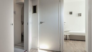 A modern, minimalist bedroom with a bed, a small stool, and a white wall with a picture. - Italianway Easy - Volta 21 (Milan)