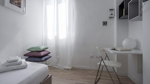 A bedroom with a bed, a desk, and a chair. There is a window with sheer curtains, a wall-mounted shelf, and a wall-mounted light fixture. - Italianway Easy - Volta 21 (Milan)