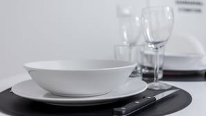 A white bowl on a plate with a knife beside it, set on a table with a black placemat. - Italianway Easy - Volta 21 (Milan)